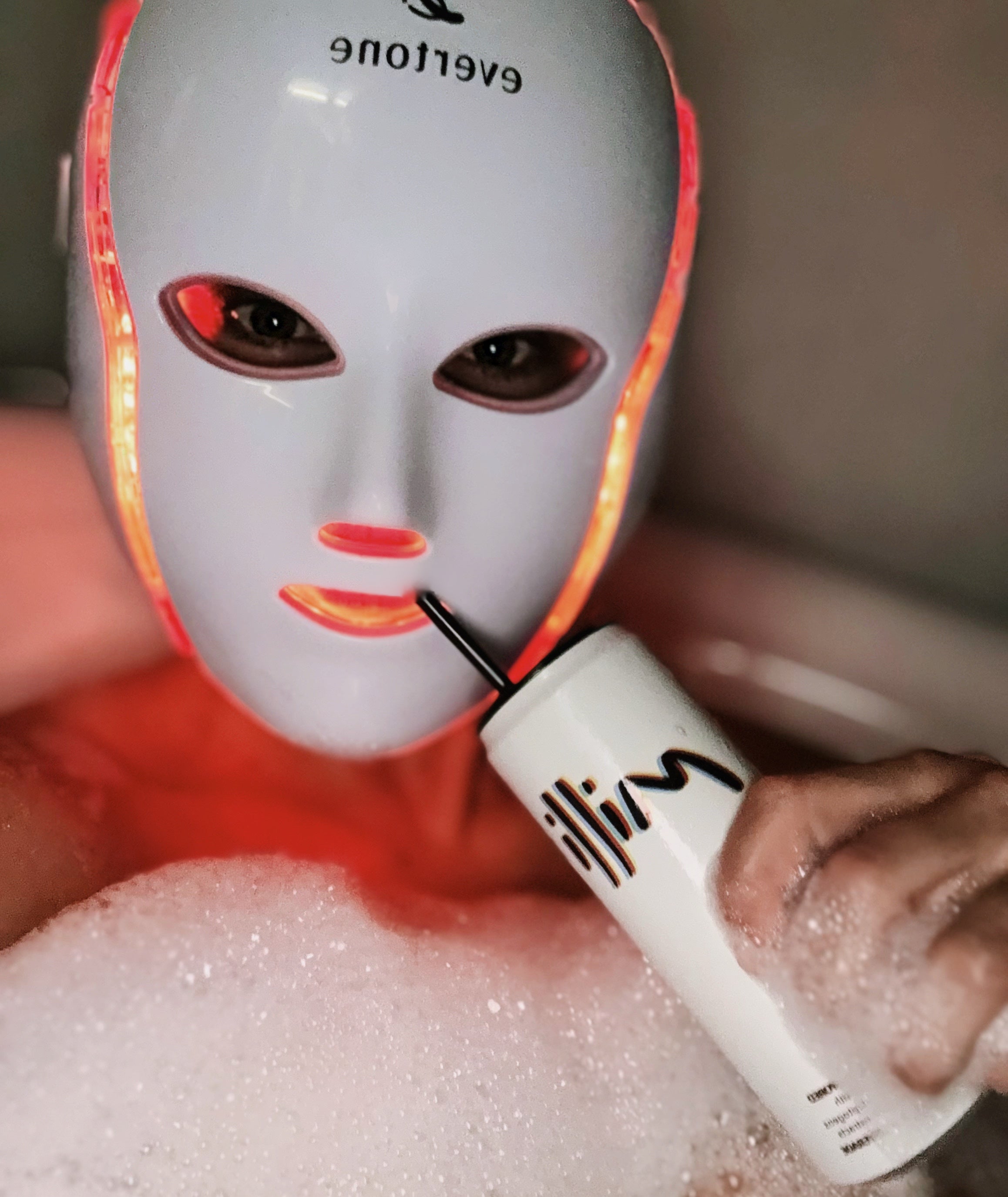 Person using a LED face mask with a handheld device, likely for skincare treatment.