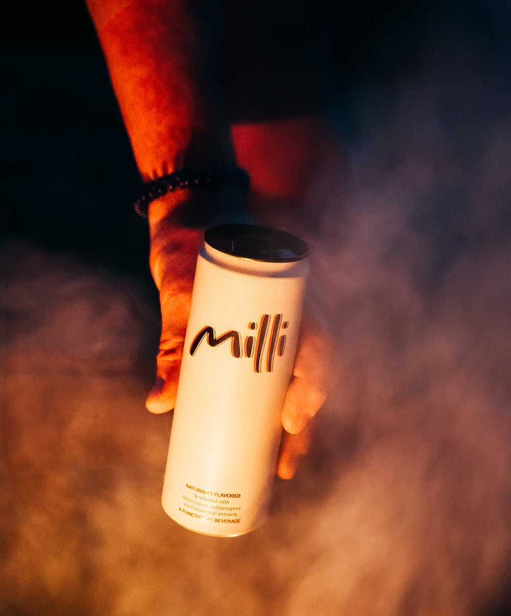 A can of Milli held up through campfire smoke at night
