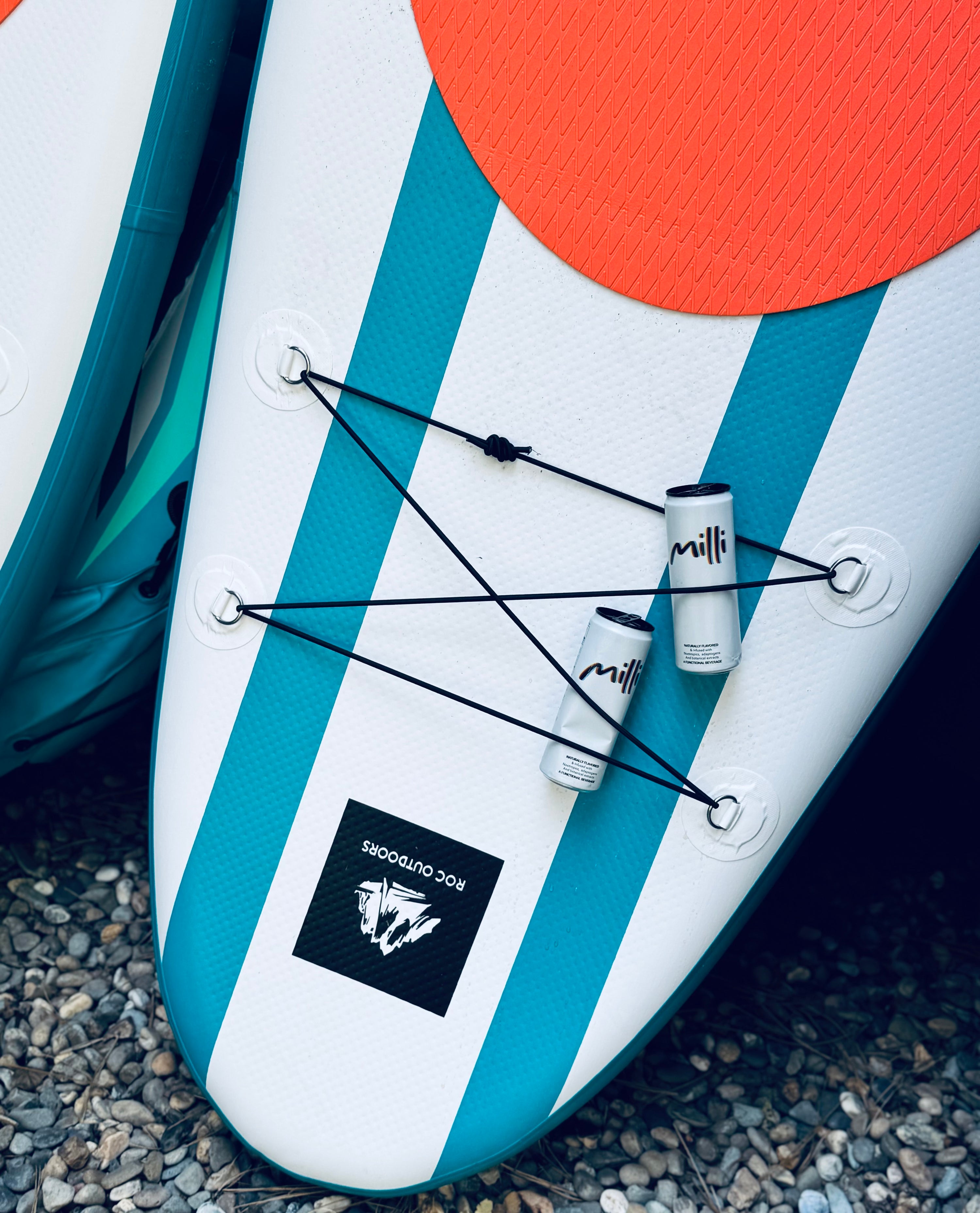 Inflatable stand-up paddleboard with blue and white stripes and orange circle on a gravel surface