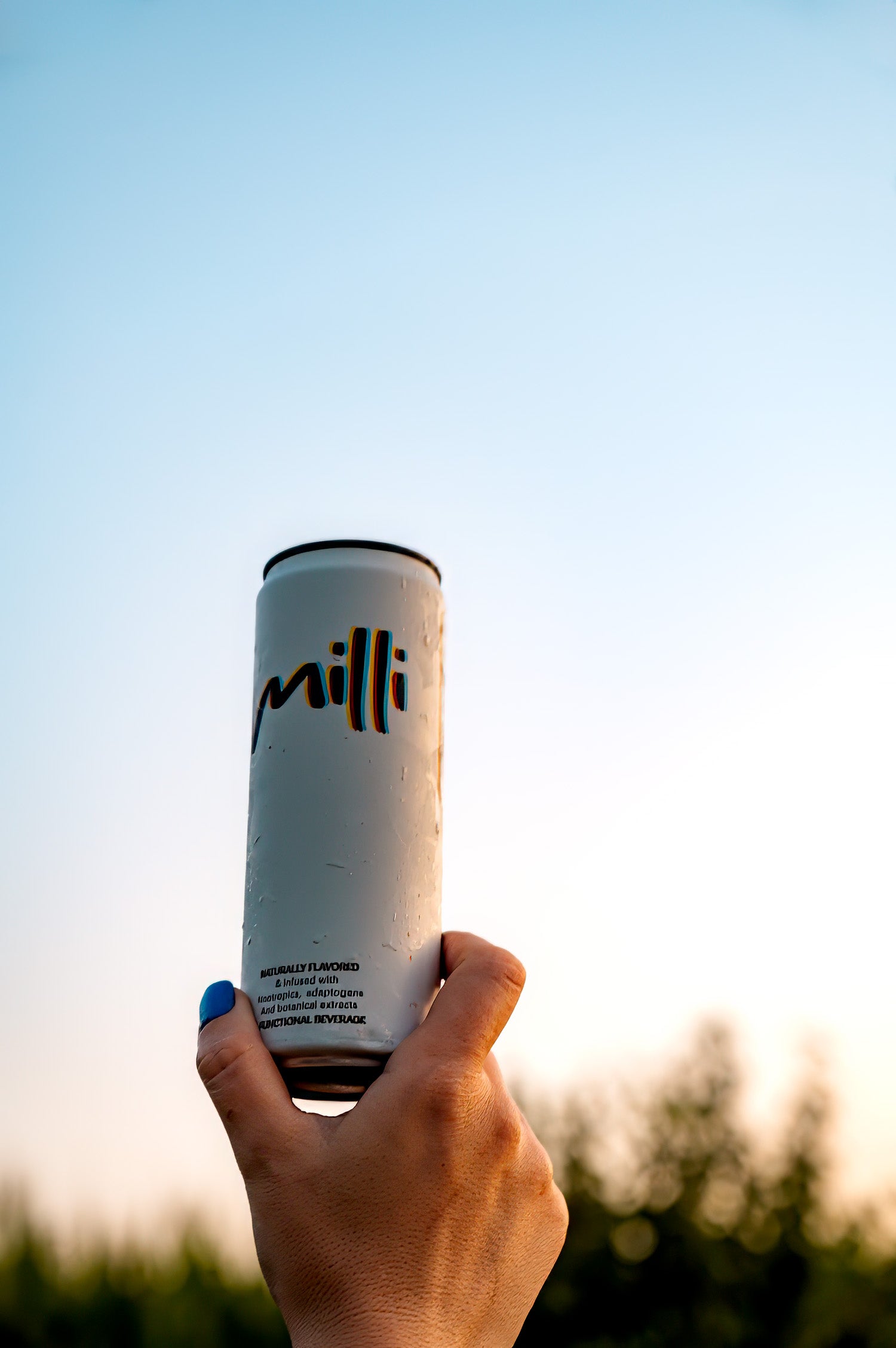 Hand holding a cylindrical container with 'milli' branding against a blurred natural background